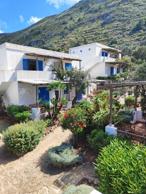 Traditional Mediterranean-style building with a flat roof and lush greenery surroundings, offering scenic views of the mountains.