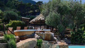 A pool with a natural rock design, surrounded by lounge chairs and a thatched-roof structure. - Marettimo Residence (Marettimo)