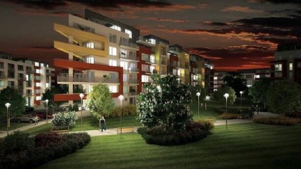 A multi-story residential building with balconies, surrounded by well-maintained lawns and street lamps.