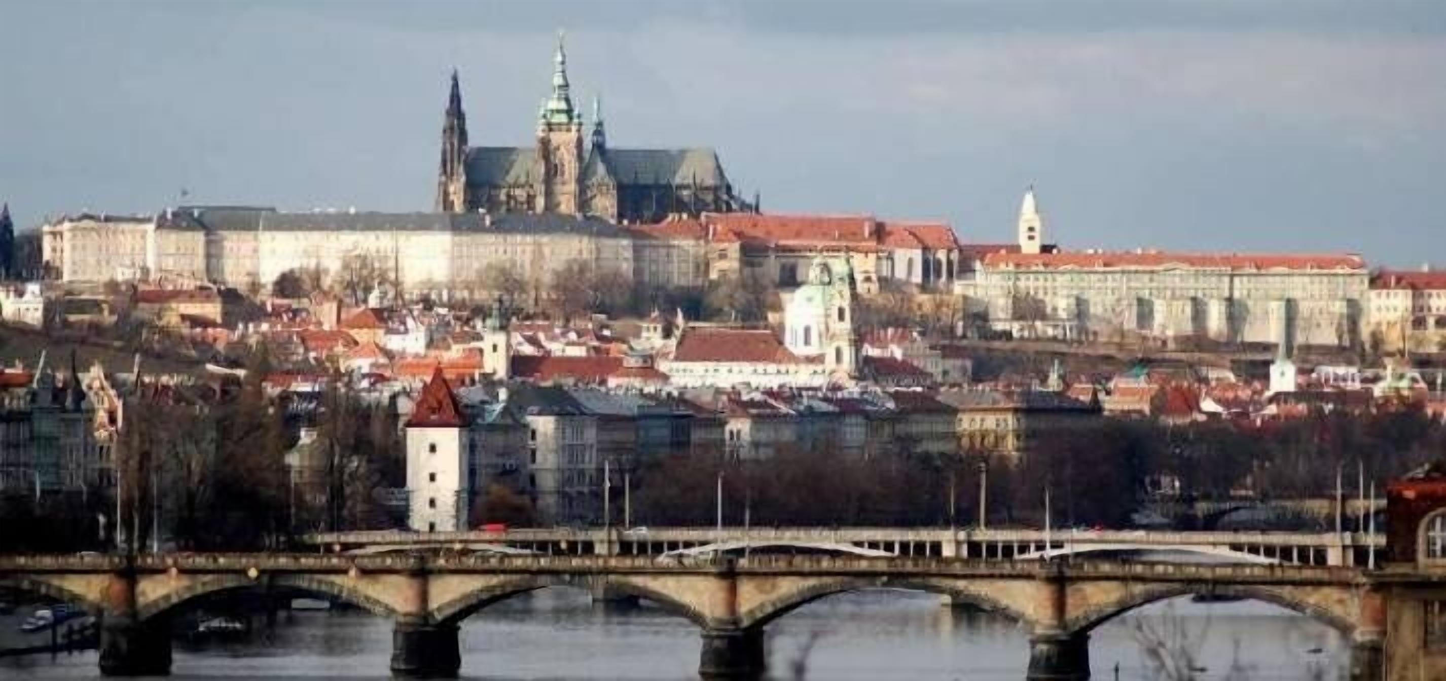 Un paisaje urbano histórico con una imponente estructura similar a un castillo y un puente que cruza un río.