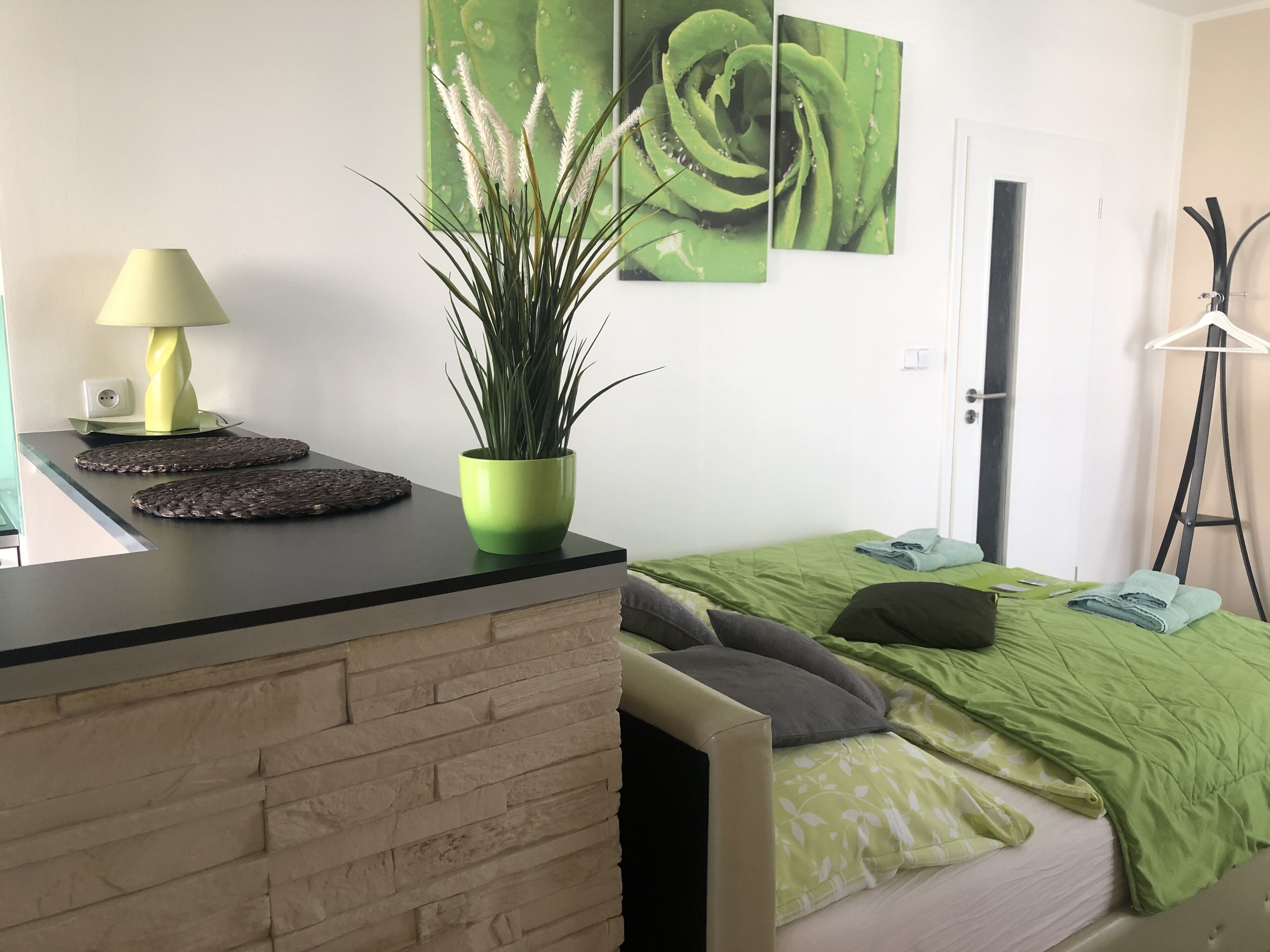 Une chambre à coucher avec un lit, une plante verte, une lampe et un mur orné d’un motif floral vert.