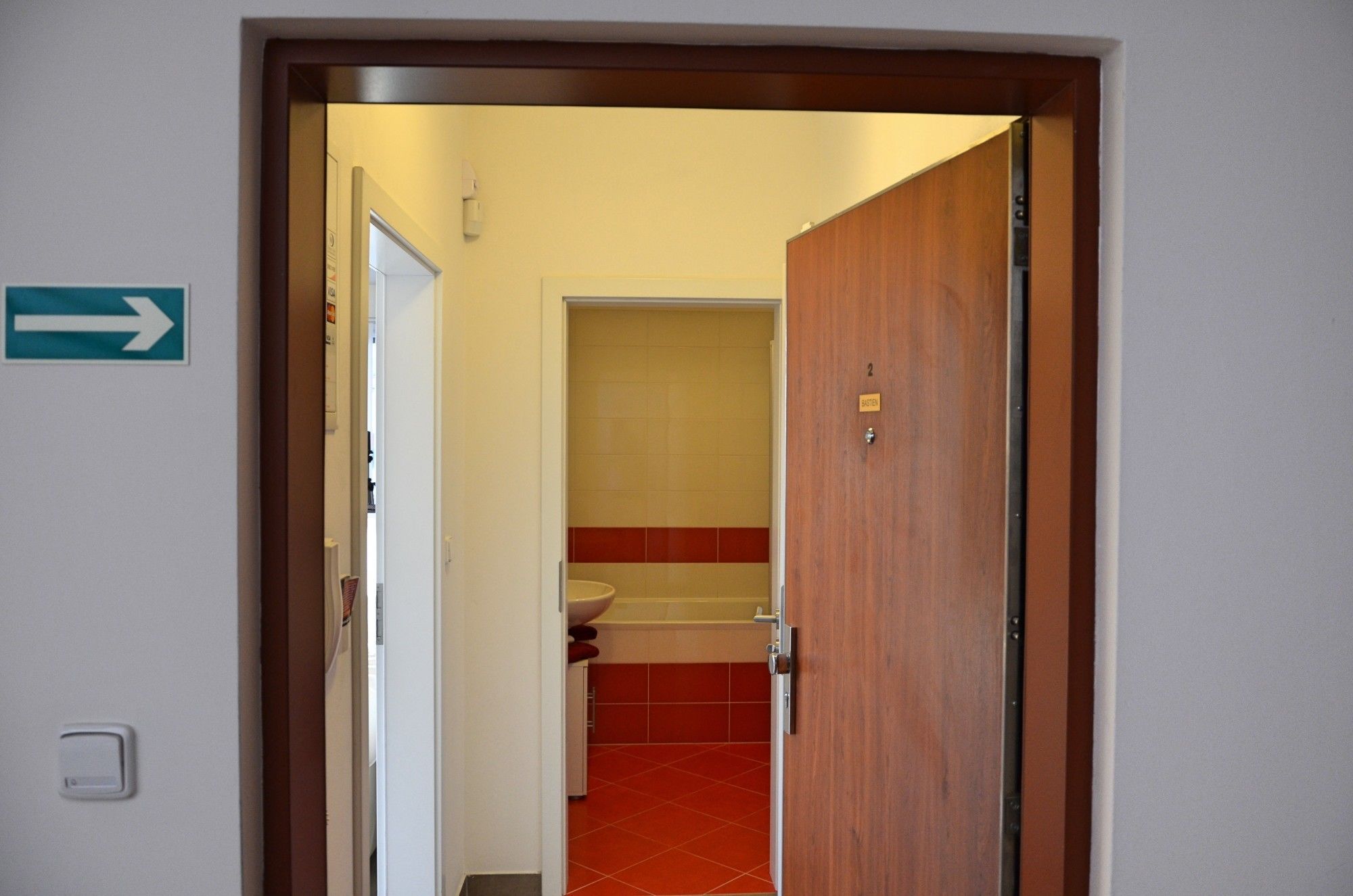 A hallway leading to a bathroom with a red-tiled floor and a sink.