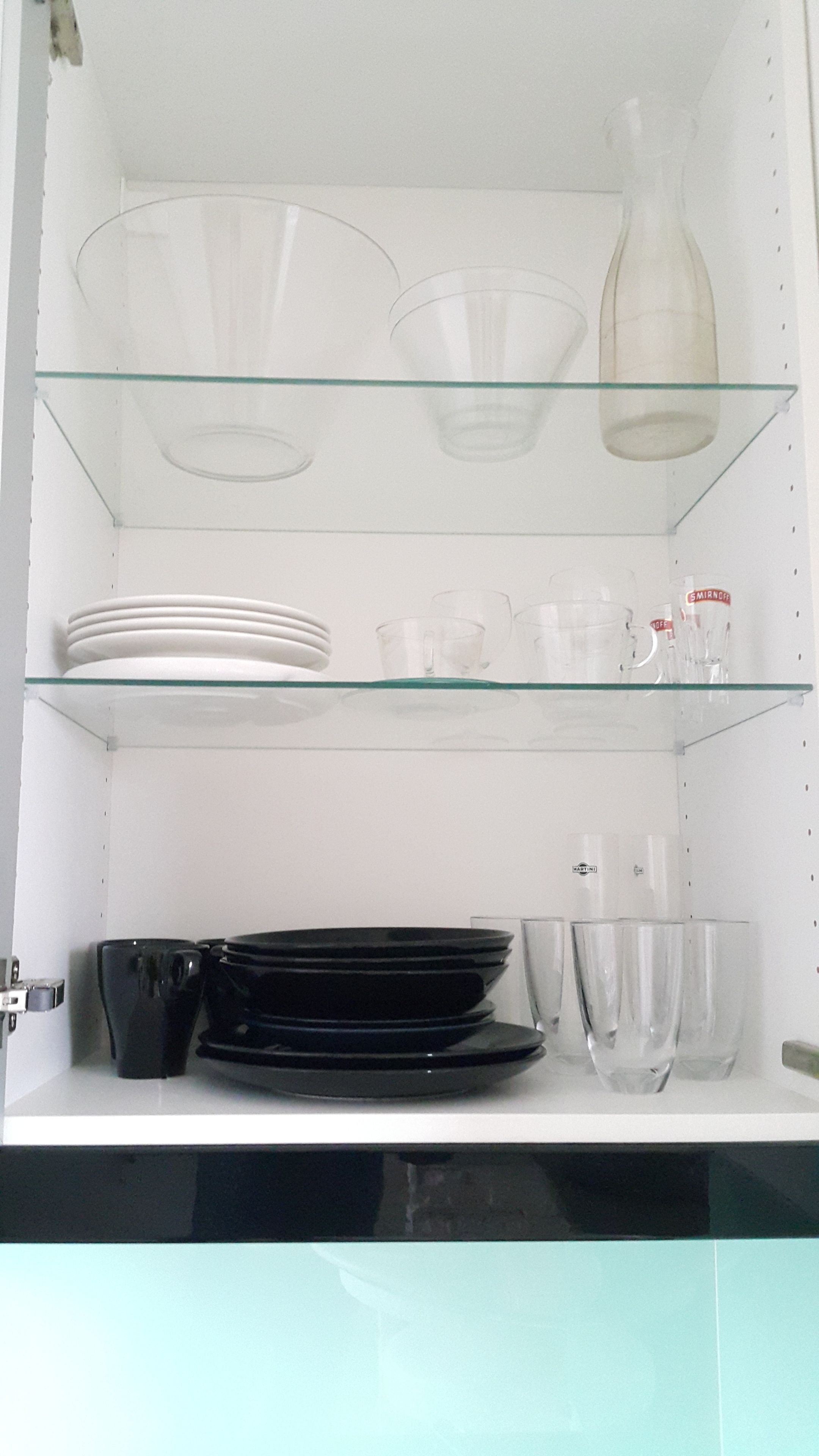 A kitchen cabinet with glass shelves holding plates, bowls, and glasses.
