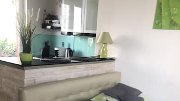 A bedroom with a bed, green and white bedding, a green rug, a small kitchen area with a stove, and a window.