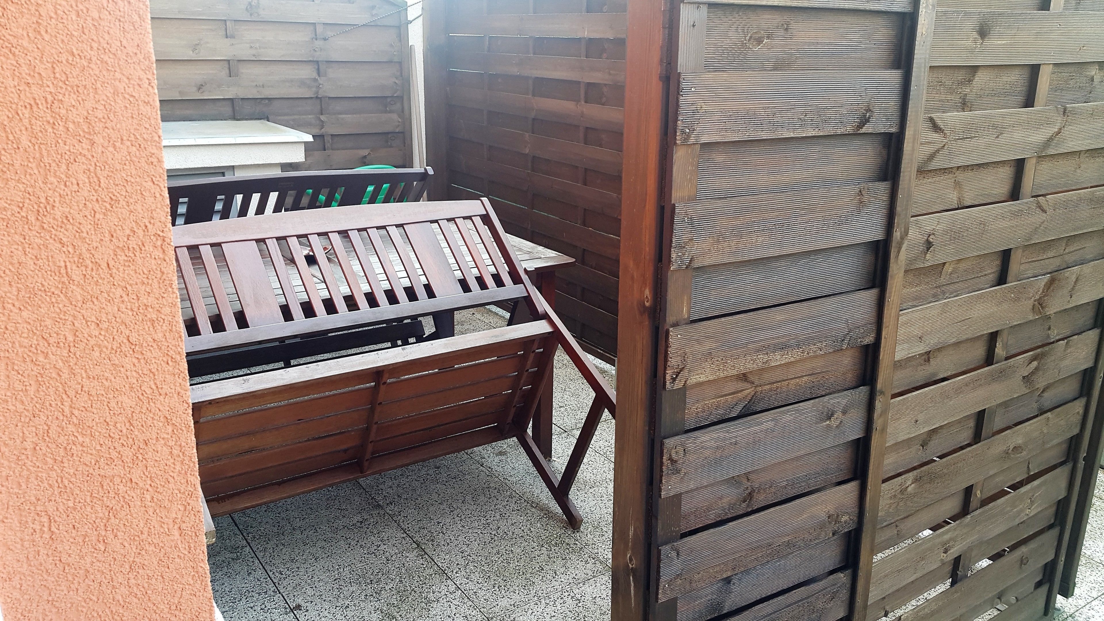 A wooden outdoor seating area with a table and benches, enclosed by a wooden fence.