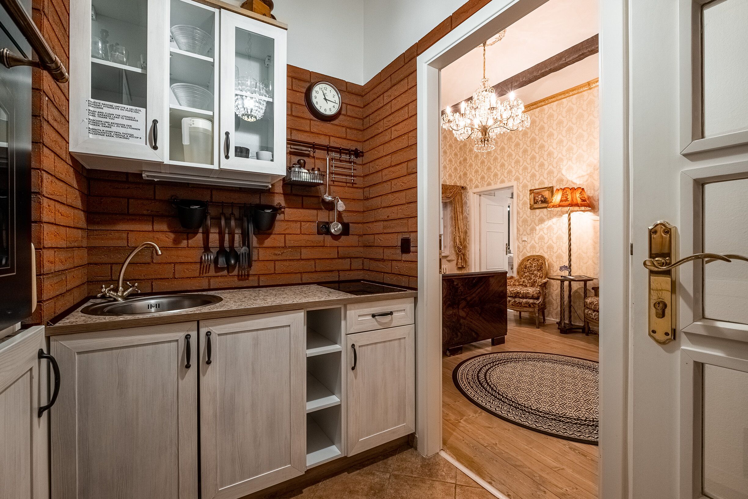 A kitchen with a brick wall, white cabinets, and a clock.