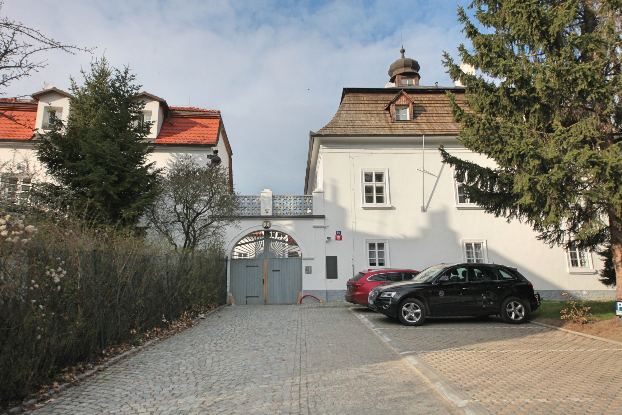 A building with a gated entrance, parked cars, and a cobblestone driveway.