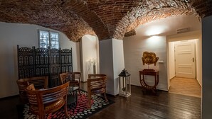 Una habitación con techo de ladrillo, sillas de madera, alfombra estampada y un jarrón decorativo.