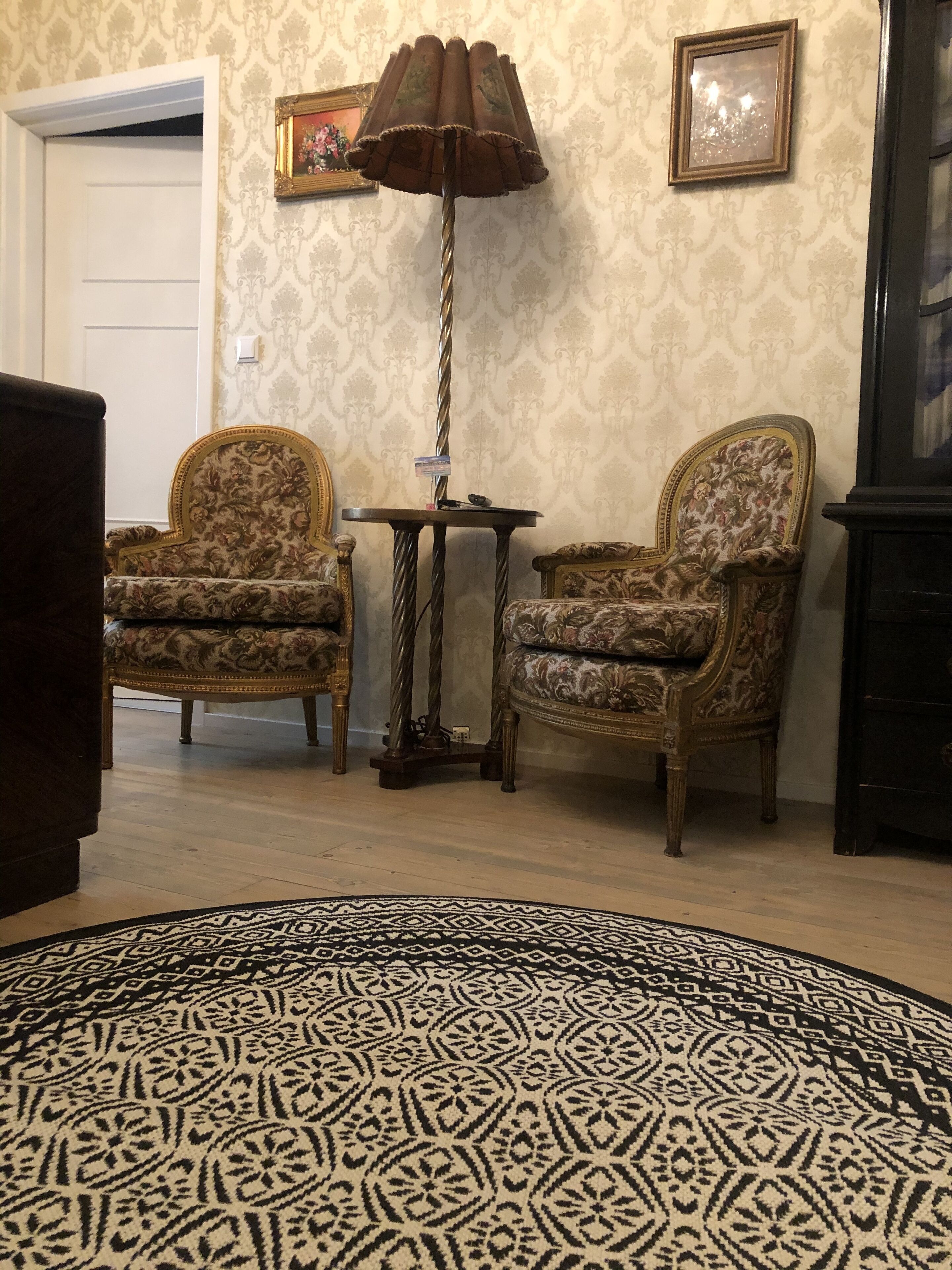 A room with two patterned armchairs, a floor lamp, a small table, and a patterned rug.