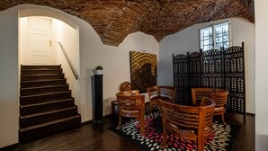 Una escalera conduce a una habitación con techo de ladrillo, sillas de madera, alfombra estampada y un adorno en la pared.