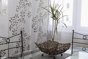 Uma planta em vaso sobre uma mesa de vidro com cesto decorativo, em frente a uma parede com padrão floral.