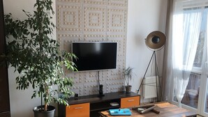 Ett vardagsrum med en platt-TV, en takfläkt, en krukväxt, ett soffbord och en soffa klädd i läder.