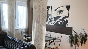 Ett vardagsrum med en svart lädersoffa, ett matbord med stolar, en krukväxt och en stor, abstrakt tavla på väggen.