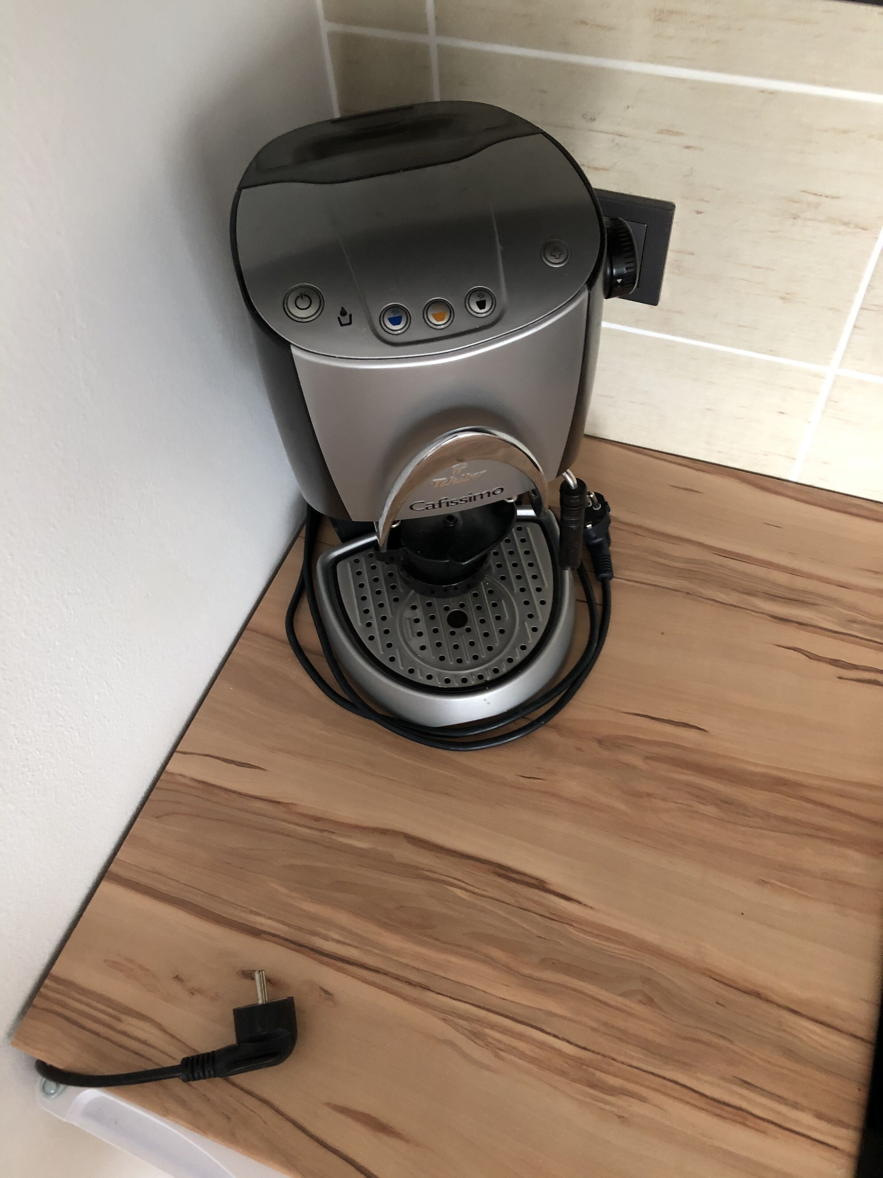 Une machine à café posée sur un comptoir en bois, avec un câble d’alimentation.