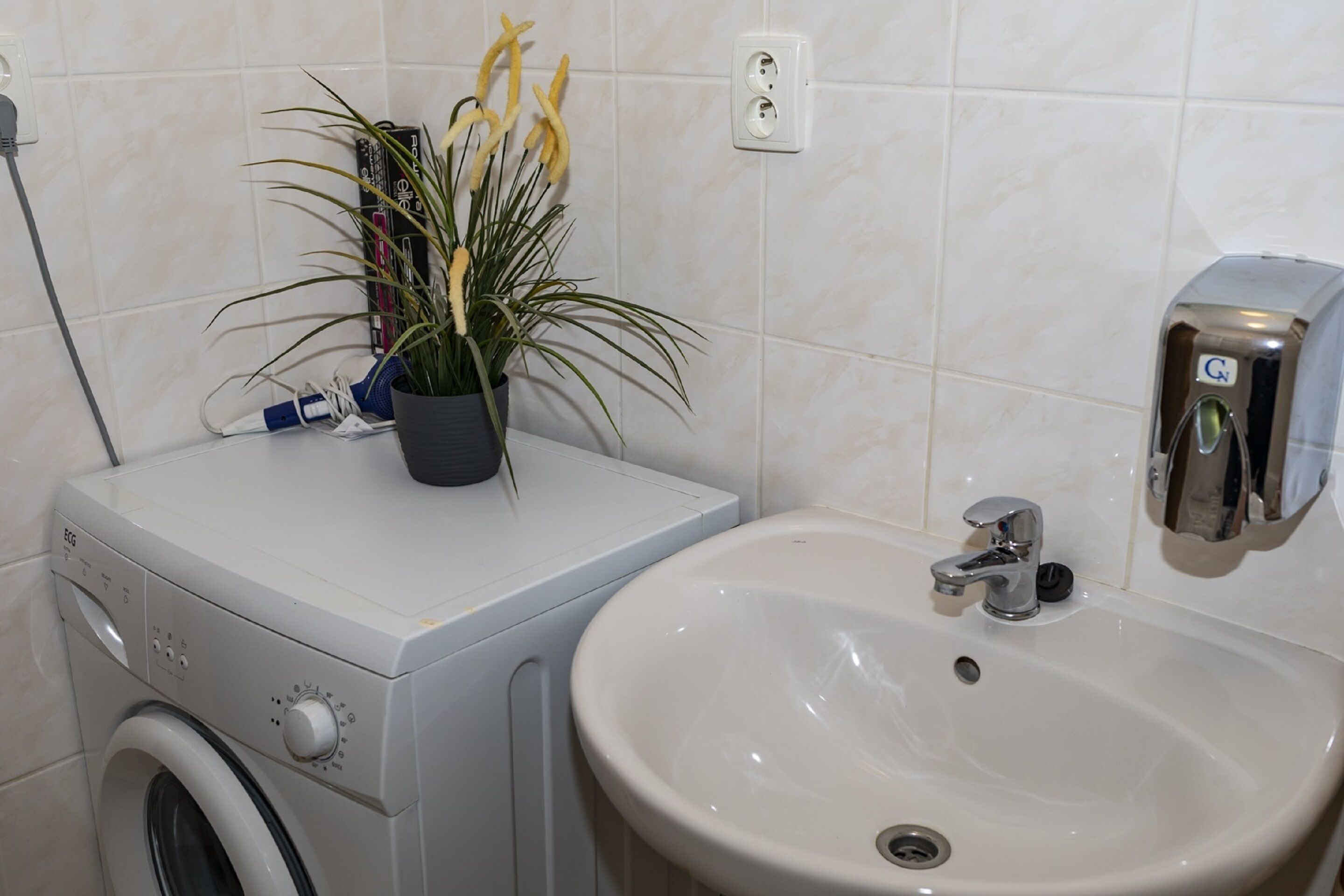 A compact bathroom with a washing machine, a sink, and a hand dryer.