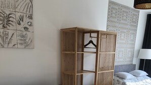 Ett modernt, väl upplyst rum med en mörkgrå soffa, ett litet runt bord, en trägarderob och en säng med mönstrat sänglinne.