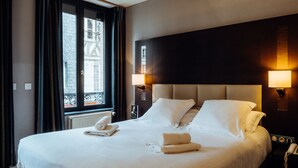 Habitación de hotel con una cama grande, dos lámparas de noche, un teléfono y una ventana con cortinas.