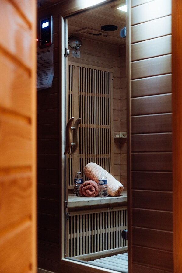 A sauna room with a wooden door, a towel, and a bottle of water on a shelf. - Hotel le Dauphin les Loges (Honfleur)