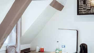 Un dormitorio acogedor y pequeño en el ático, con techo inclinado, un escritorio con silla, un radiador, una lámpara y una obra de arte en la pared.