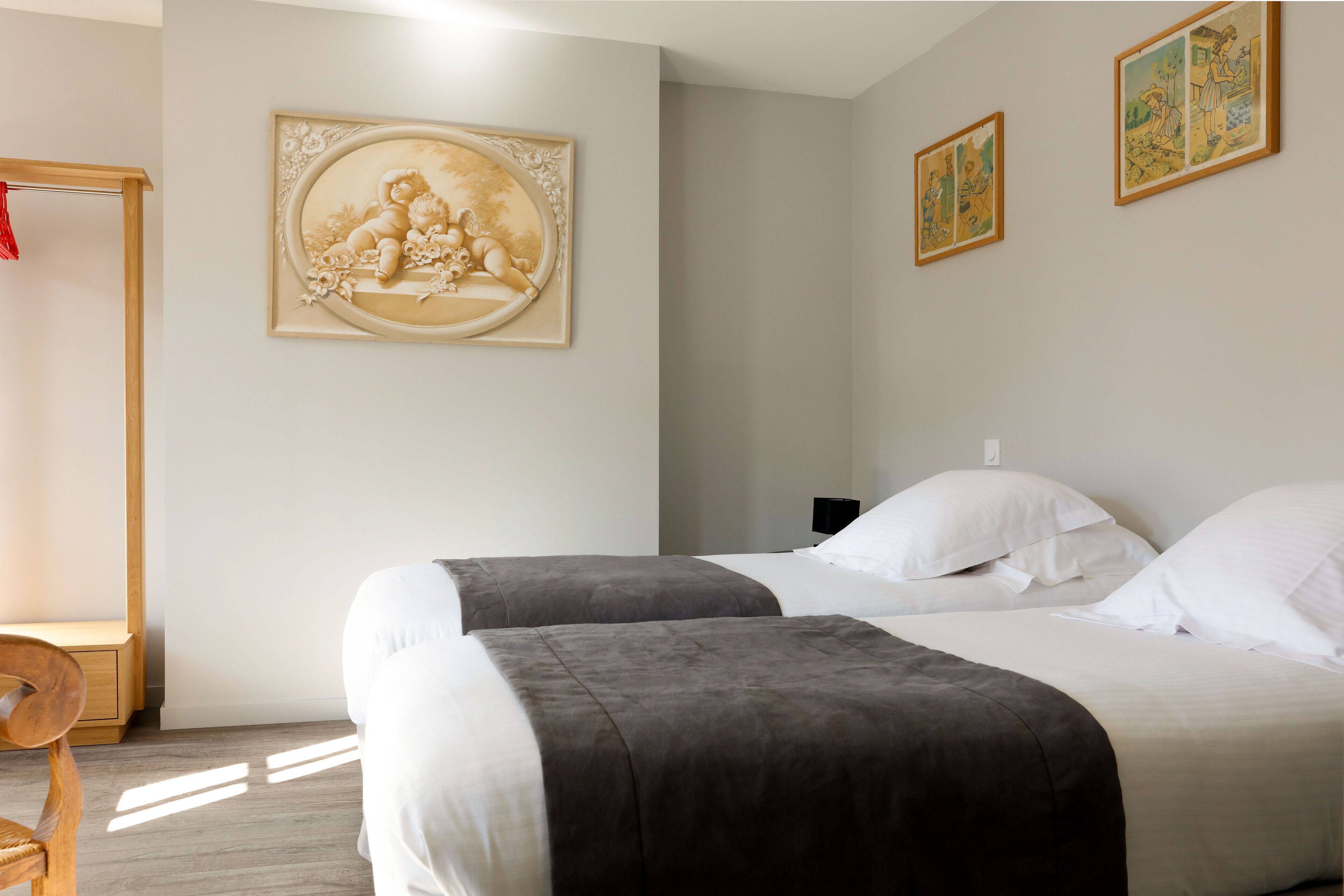 A bedroom with two beds, a wooden chair, and wall-mounted artwork.