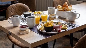 Una mesa de desayuno con diversos alimentos, como cruasanes, queso y un bol de fruta.