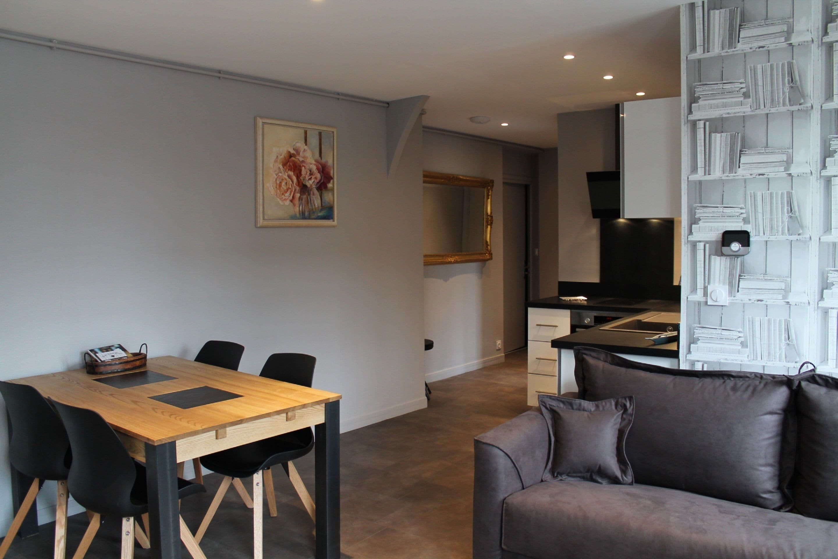 Een moderne woonkamer met een houten eettafel, zwarte stoelen, een grijze bank en een boekenkast vol boeken.