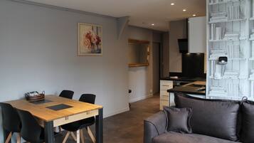 Een moderne woonkamer met een houten eettafel, zwarte stoelen, een grijze bank en een boekenkast vol boeken.
