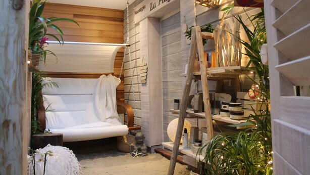 Un área de spa con un sofá blanco, estantes de madera con productos de spa y una lámpara colgante.