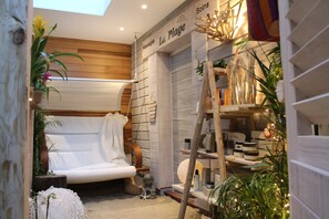 Un área de spa con un sofá blanco, estantes de madera con productos de spa y una lámpara colgante.