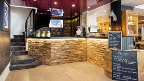 Interior de restaurante con mostrador de piedra, escalera de madera y menú en una pizarra.