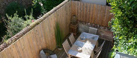 Eine Holzterrasse mit Tisch und Stühlen, umgeben von einer Steinmauer und Grünpflanzen.