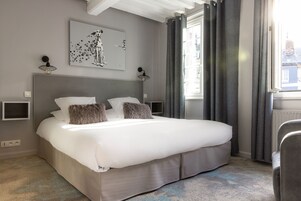 Una cama bien hecha con cabecera gris, dos mesitas de noche y una obra de arte colgada en la pared.