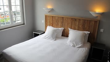 Una cama bien hecha con sábanas blancas y dos almohadas, un cabecero de madera y dos lámparas fijadas a la pared.