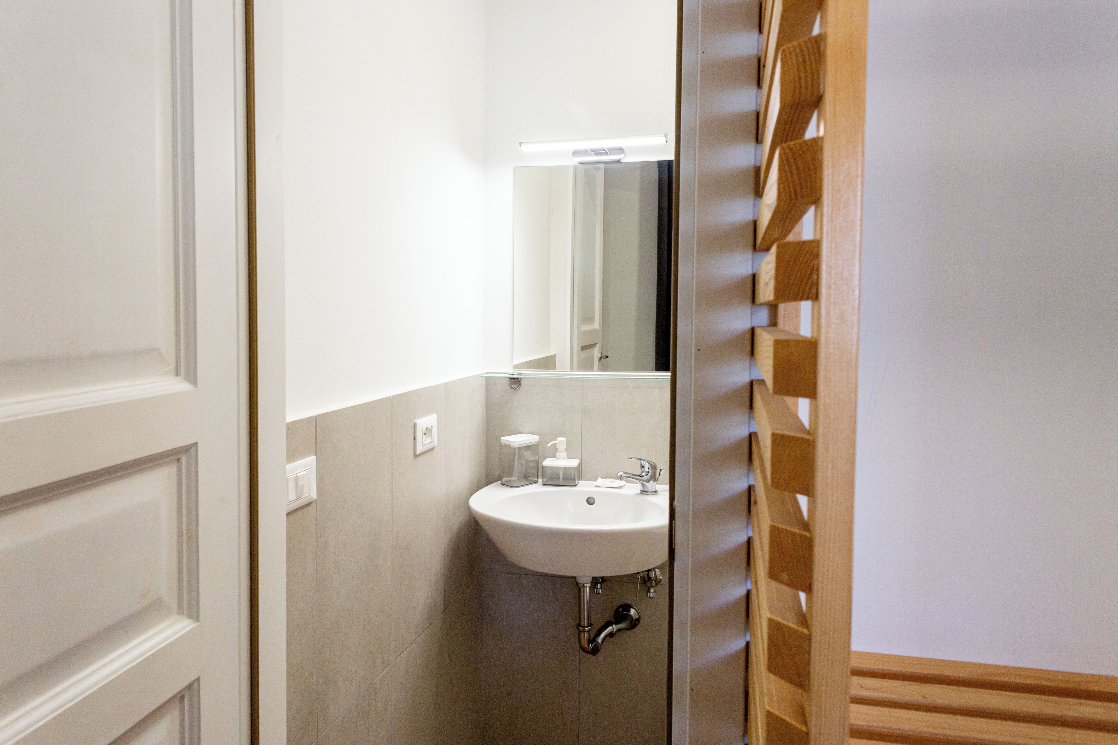 A bathroom with a white sink, mirror, and wooden slatted door.
