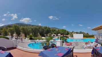 A poolside area with a view of a mountain, outdoor seating, and a swimming pool.