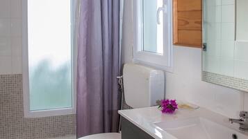 Ein Badezimmer mit Holzboden, einer weißen Toilette, einem Waschbecken mit Spiegel und einer Duschkabine mit lila Vorhang.