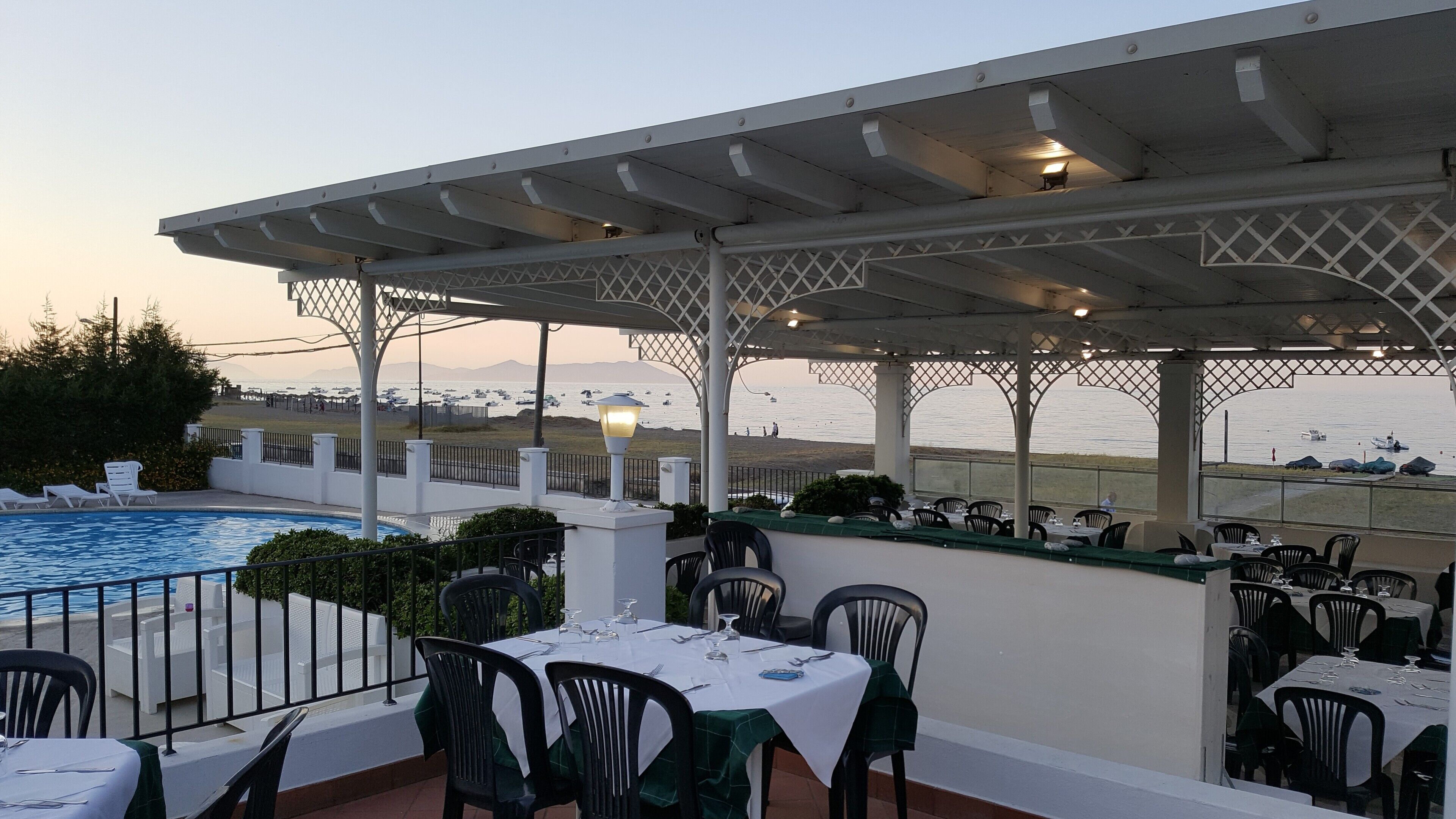 Un área de comedor al aire libre con mesas y sillas, piscina y vista al mar.