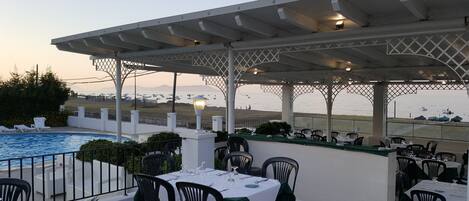 Un área de comedor al aire libre con mesas y sillas, piscina y vista al mar.