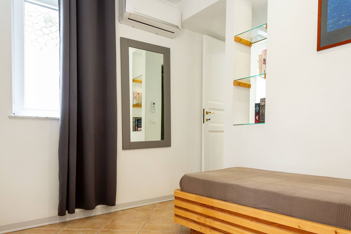 Een slaapkamer met een bed, een raam met gordijnen, een airconditioner en een spiegel.