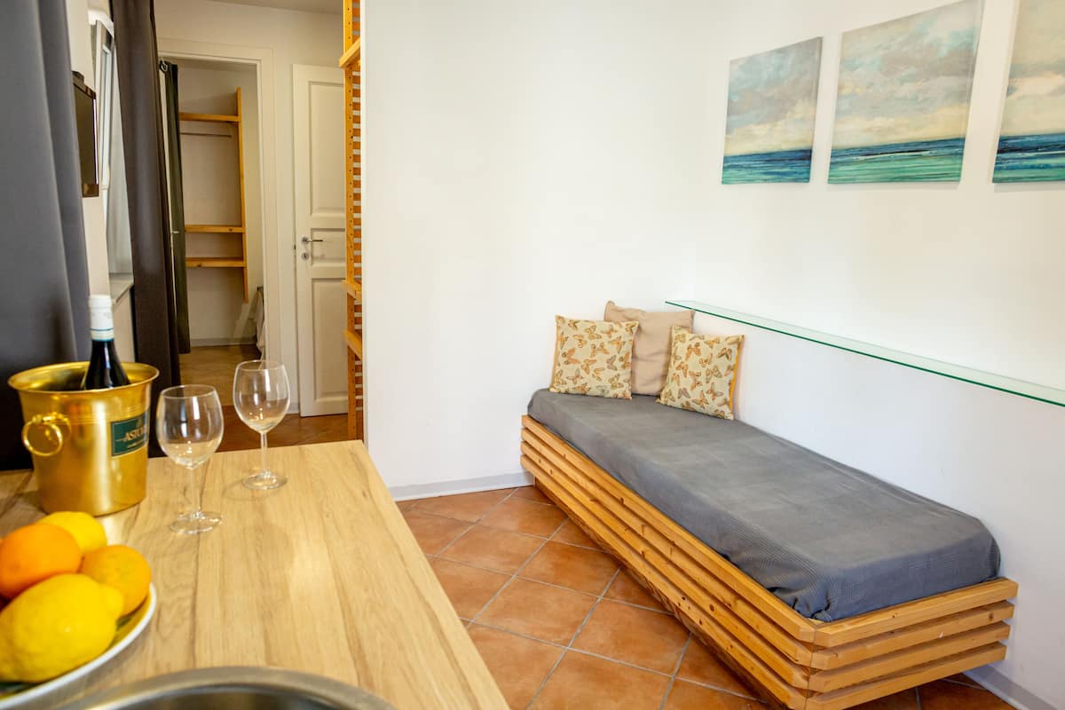 Een compacte kamer met een bed, een klein tafeltje met een fles en glazen, en een schaal fruit.
