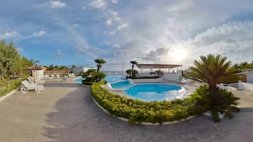 Un área de piscina con varias piscinas, sillas de descanso y palmeras.