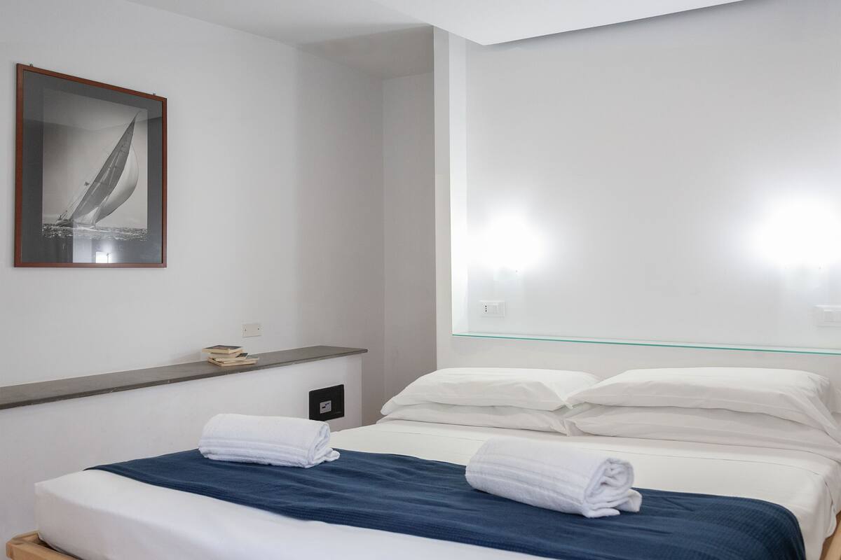 Een moderne hotelkamer met een bed, een glazen hoofdbord en een ingelijste foto aan de muur.