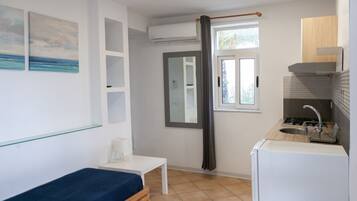 A compact room with a bed, a small table, a window with a view, a kitchenette, and a mirror.