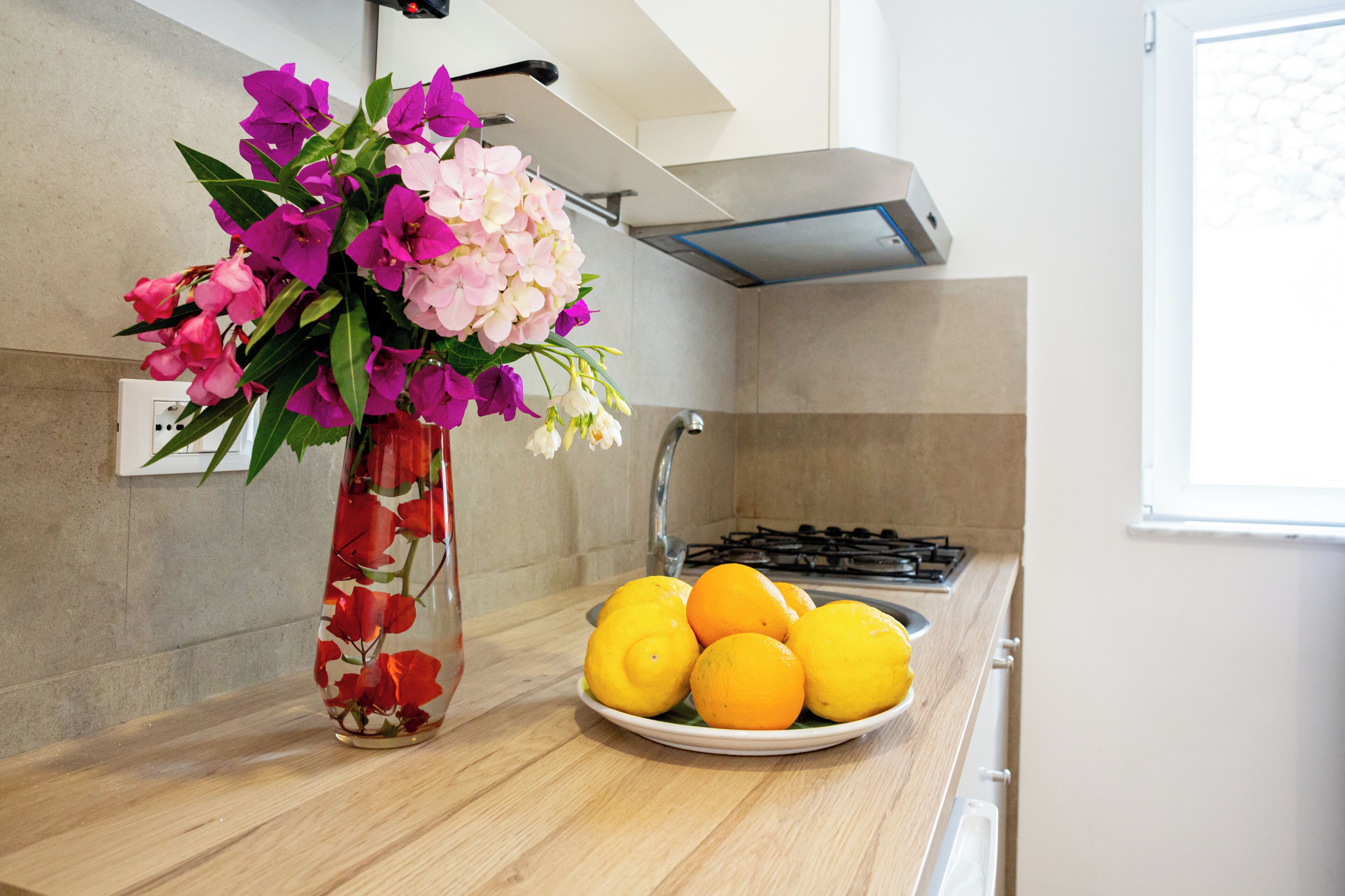 A kitchen counter with a vase of flowers and a plate of oranges.