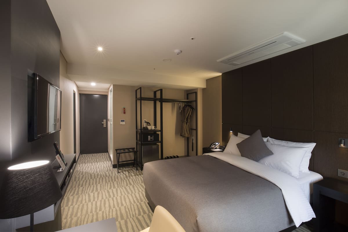Une chambre d’hôtel avec un grand lit, une table de chevet, une lampe, une armoire et un miroir.