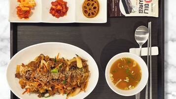 A tray with a plate of beef stir-fry, kimchi, and a soup bowl, along with a packaged snack.