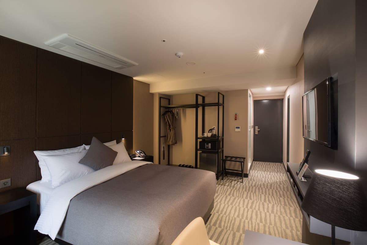 Une chambre d’hôtel avec un grand lit, un bureau, une chaise, une armoire et un miroir.