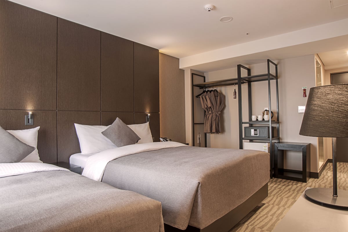Une chambre d’hôtel moderne équipée de deux lits, d’une armoire, d’un bureau et d’une lampe.
