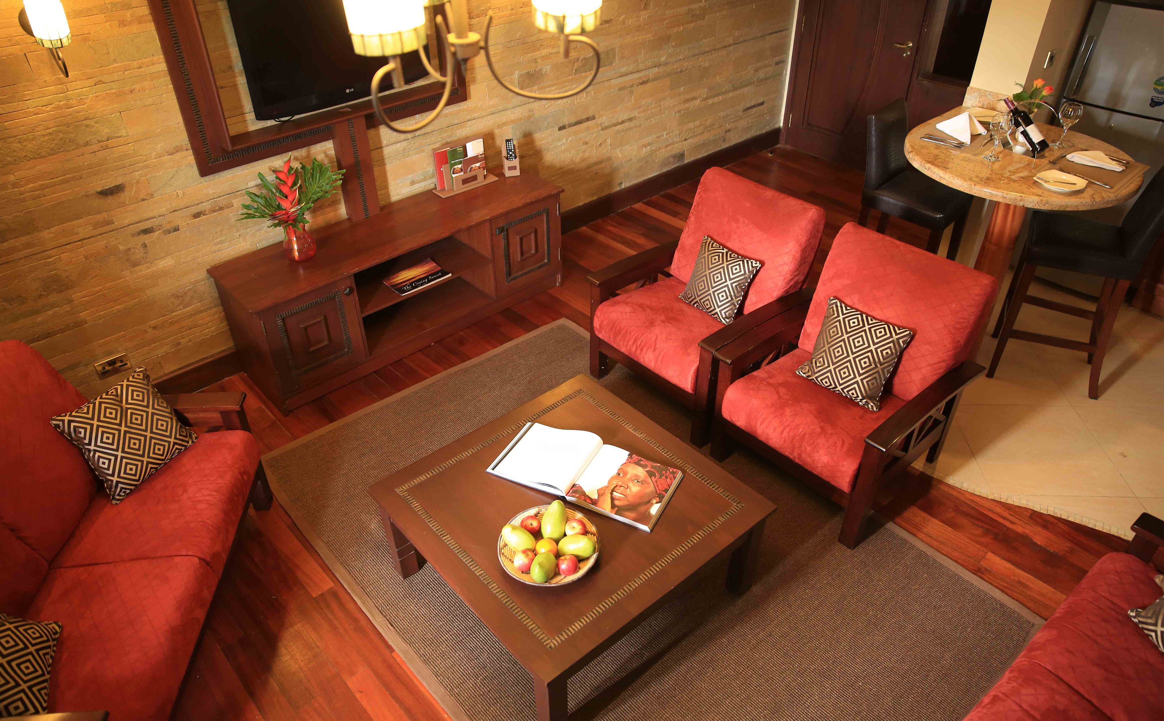 Een gezellige woonkamer met een houten vloer, rode banken, een salontafel met een fruitschaal, een televisie en een klein zithoekje met een tafel en stoelen.
