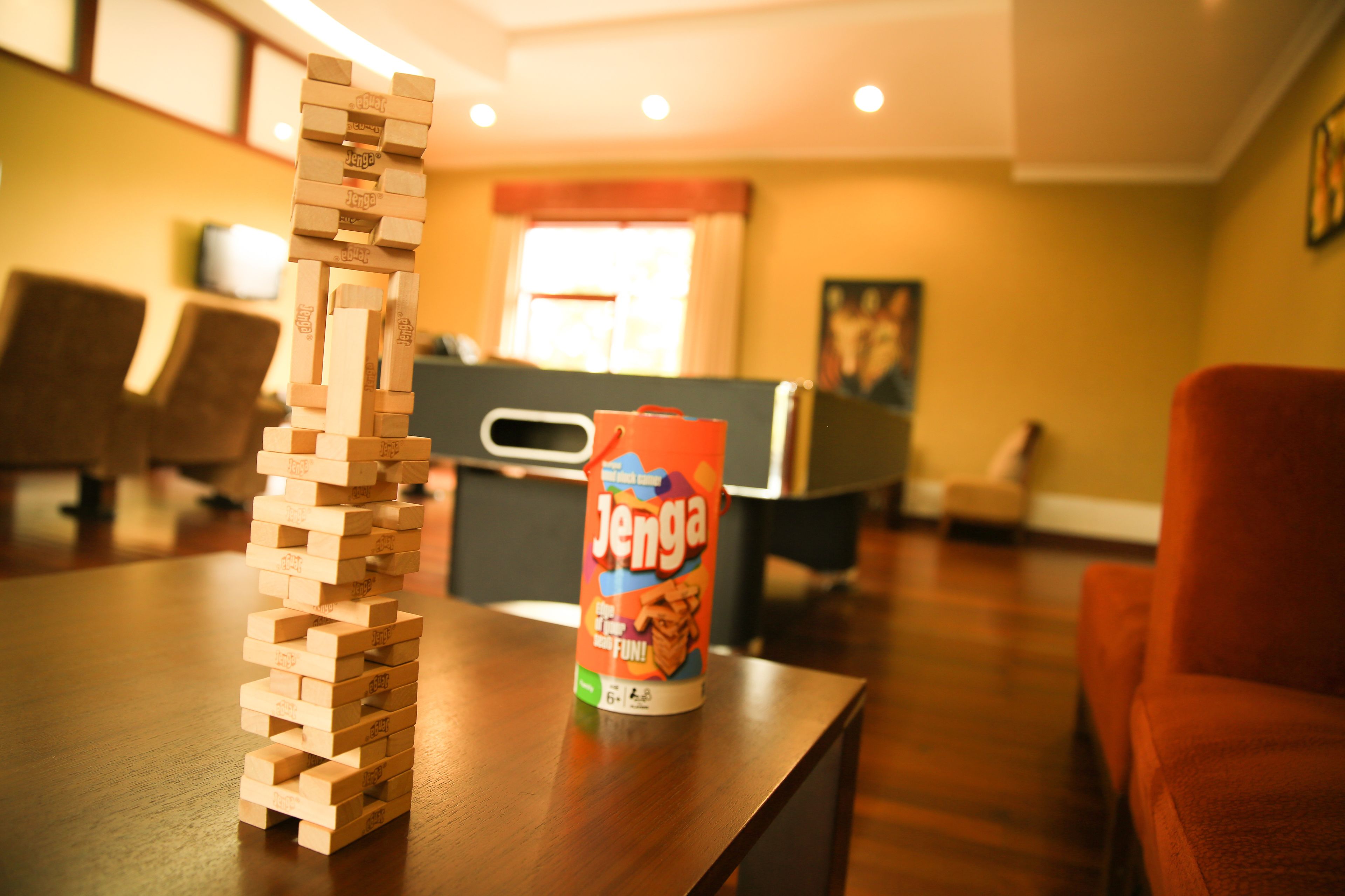 A wooden Jenga tower on a table with a can of Jenga in the background.